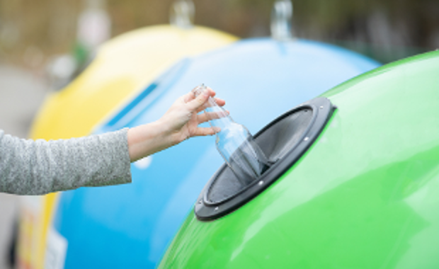 Hand putting clear glass bottle into a recycling container