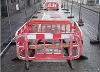 Photograph showing temporary road barriers around a hole in the road through which can be seen a layer of concrete overlayed by a timber bar